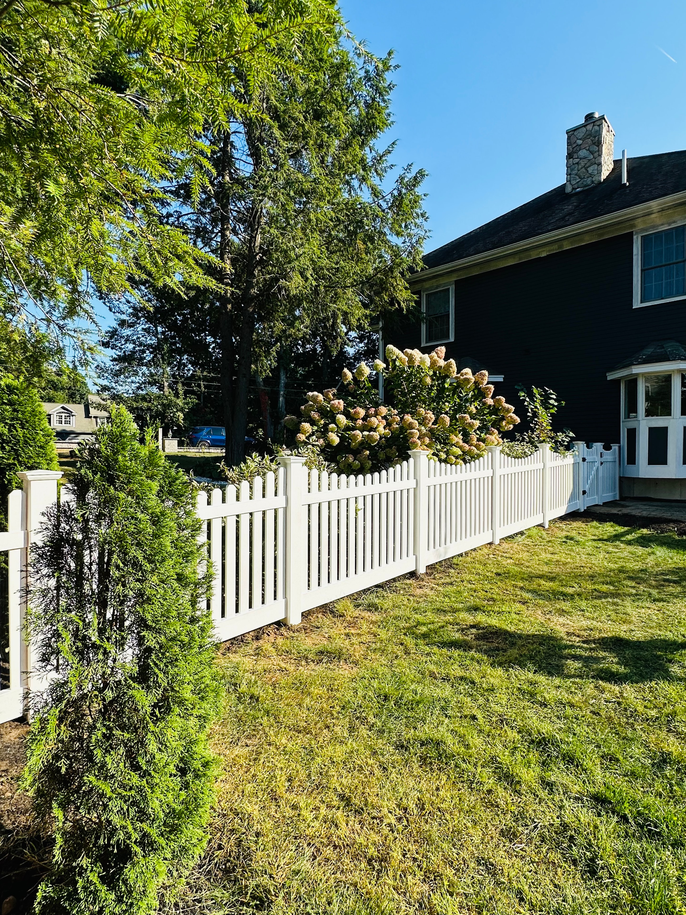 White vinyl picket fence with hydrangeas by Ultra Fence LLC